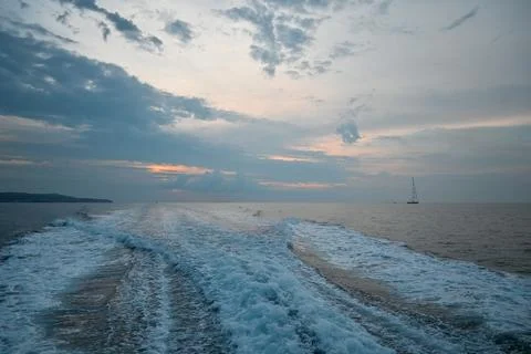 Waves trailing behind a moving boat on the sea at dusk Stock Photos
