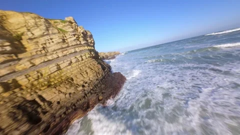 Waves tumble over rugged coastal rocks beneath bright blue sky at Peniche Video stock 346076156