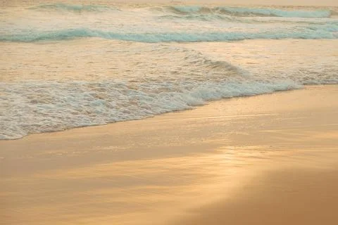 Waves wash ashore on sandy beach during evening light near ocean. Waves roll Foto stock
