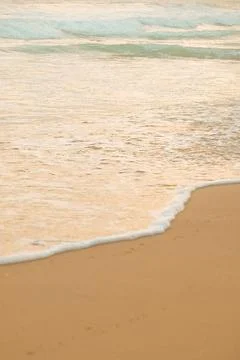 Waves wash ashore on sandy beach during evening light near ocean. Waves roll Stock Photos