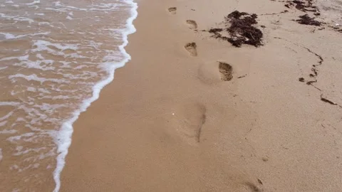 Waves wash away the traces of bare feet on the sand 库存影片 338529961