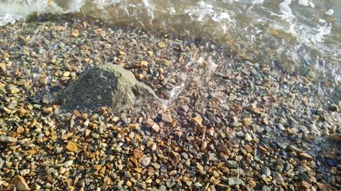 Waves wash over the pebble beach. Sea surf close-up. Clear ocean water with foam Stockbeeldmateriaal 252144121