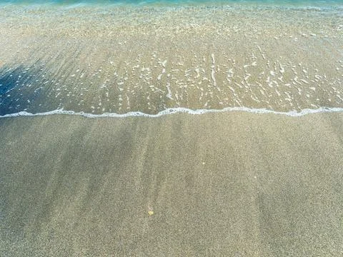 Waves wash over a sandy beach creating a line where water meets land during.. Stock Photos