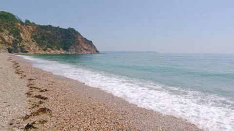 Waves Wash Over Shingle Beach Showing Steep Coastal Cliffs Under Bright Blue Sky Stock Footage 337490531