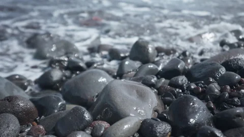 Waves wash over smooth rocks on a serene beach shoreline at low tide Video stock 328031386