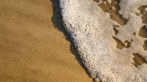 Waves wash onto a sandy beach during the day near the shore Stock Photos