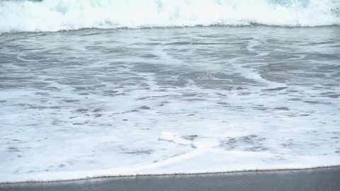 Waves washing up onto a dark sand beach Video stock 74288462