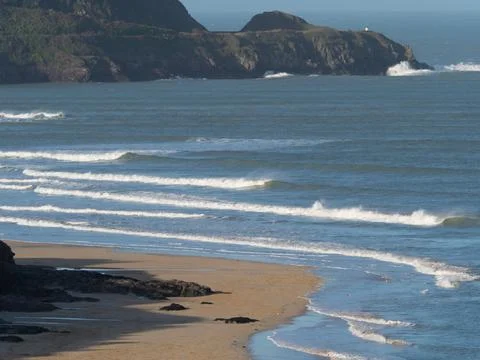 Waves with white tops break onto a sandy beach with a rocky headland Stock Photos