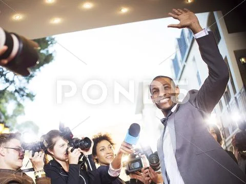 Waving celebrity being interviewed and photographed by paparazzi at event Stock Photos