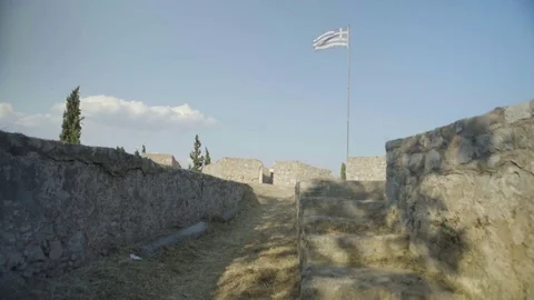 Waving flag of Greece in front of medieval fortress wall Stock Footage 77453703