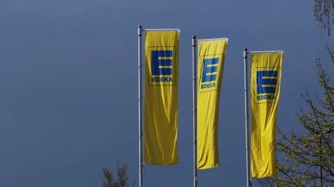 Waving flags with Edeka Group logo against the dark blue sky Stock Footage 152974584