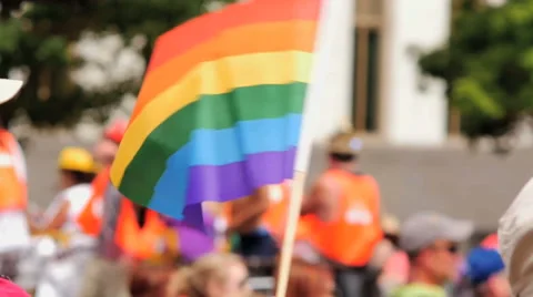 Waving Rainbow flag with float of gay pride supporters in background slow motion Stock Footage 51511473