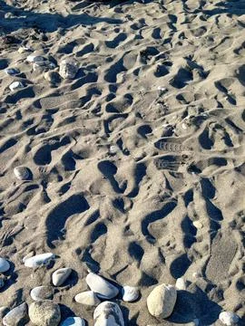Wavy sand patterns with footprints and stones on beach Stock Photos