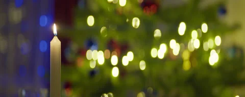 A wax candle is burning on the background of a Christmas tree with a garland Stock Footage 314833993