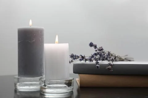 Wax candles in glass holders near books and lavender flowers on table against Stock Photos
