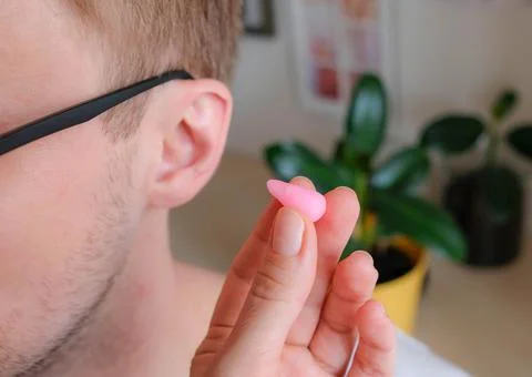 A wax earplug is molded in the form of a drop against the background of the ear Stock Photos