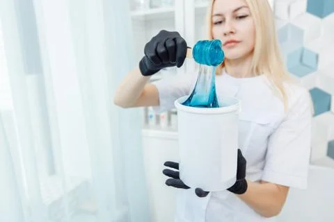 The waxing master dials a soft blue wax onto a wooden spatula. Stock Photos