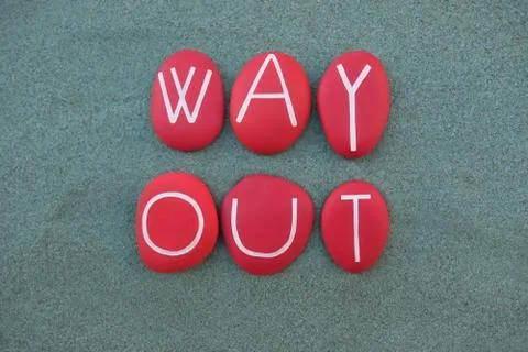 Way Out text composed with red painted stone letters over green sand Stock Photos