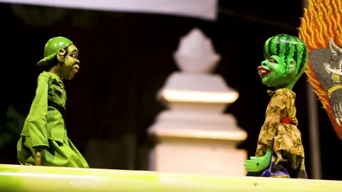 Wayang golek puppet with watermelon head whispering secretly to green unifo.. Stockbeeldmateriaal 344796758