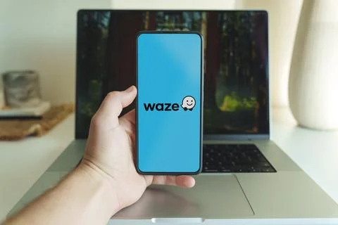 Waze navigation map application logo on smartphone screen in front of laptop Stock Photos