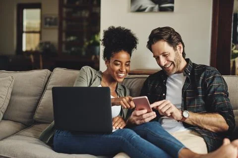 We always stay in the loop. a happy young couple using a laptop and cellphone Stock Photos