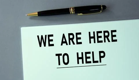 WE ARE HERE TO HELP - words on a piece of paper with a pen on a gray backgrou Stock Photos