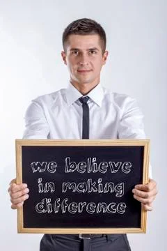 We believe in making difference - Young businessman holding chalkboard with.. Stock Photos