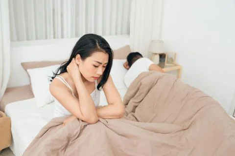 We have a problem. Young upset girl sitting on the edge of the bed, against h Stock Photos
