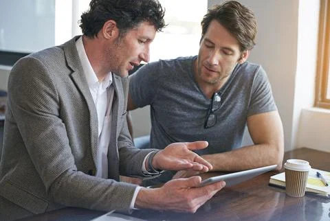 We need to tweak this app a bit. two businessmen working on a digital tablet. Stock Photos