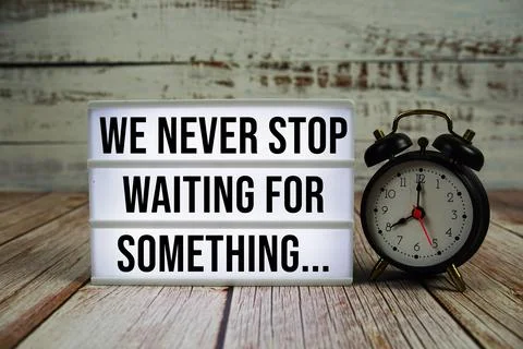We Never Stop Waiting For Something... text with alarm clock on wooden back.. Stock Photos