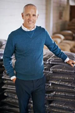 We only import the finest beans. Portrait of a mature man standing by bags of Stock Photos