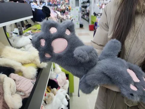 We try on fur gloves shaped like cat paws at the store Stock Photos