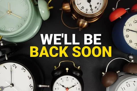 We Will Be Back Soon! text with alarm clock on black background Stock Photos