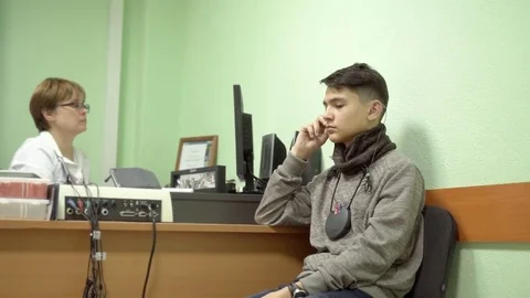 Weak-hearing young man at a doctor's appointment. The doctor adjusts the hearing Stock Footage 82519076