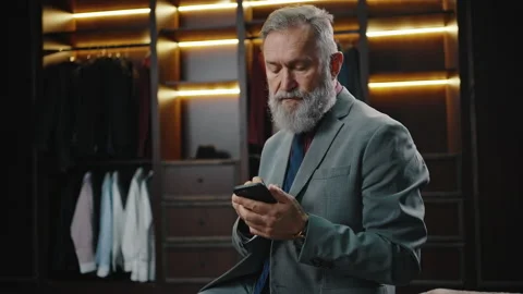 Wealthy mature bearded businessman in suit using smartphone at dressing room Stock Footage