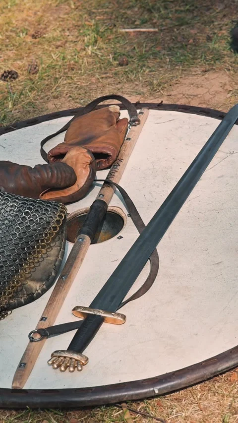Weapons and armor are arranged on a wooden round shield placed on grassy ground. Видео 345036387