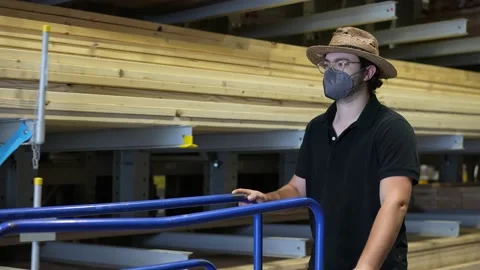 Wearing a face mask, a man pushes a lumber cart at a big box hardware store. 스톡 동영상 158377799