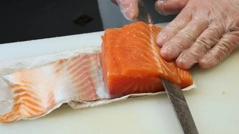 Wearing gloves, the master chef carefully slices fresh salmon into uniform Vidéo 284968125