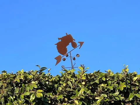 Weather vane in the shape of a tractor over green foliage Stock-Fotos