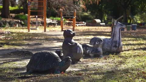 Weathered animal statues, including a turtle and a rabbit, sit in a sunny Vídeo Stock 331318135