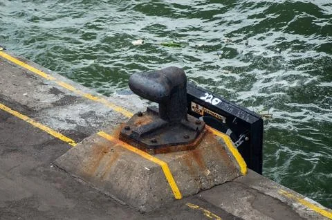 A weathered black mooring bollard with rust stands on a concrete base at ta.. Fotos Stock