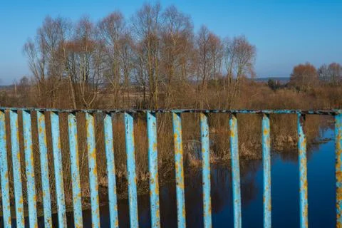 Weathered blue bridge railing frames calm river and leafless trees Stock Photos