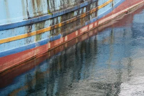Weathered Blue Red Hull of Old Fishing Boat Reflecting on Calm Harbor Water Fotos de archivo