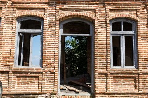 Weathered brick facade with arched windows and open doorway revealing a dark Stock Photos