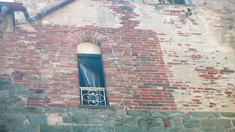 Weathered brick wall frames narrow arched window with decorative iron balcony Video stock 347478498