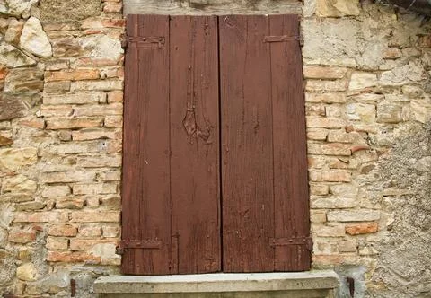 A weathered brown wooden shutter on a rustic stone and brick wall. Foto stock