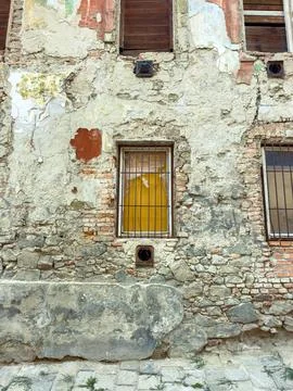 Weathered building wall shows peeling paint, exposed bricks, and a yellow win Stock Photos