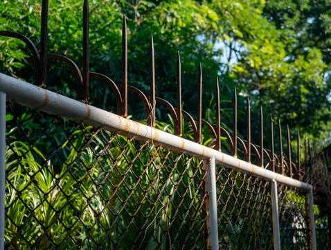 Weathered Chain Link Fence with Rusty Metal Security Spikes on Top Foto stock
