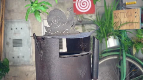 Weathered cigarette bin sits beside green bicycle beneath leafy plants. Metal 動画素材 347478914