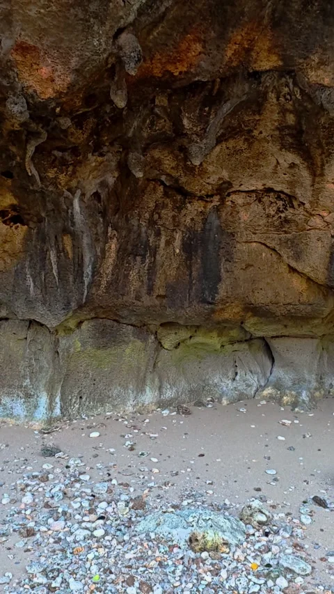 Weathered coastal cave wall above a pale pebble beach 스톡 동영상 346741214